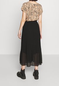 Plisovaná černá maxi sukně s průhledným lemem, spárovaná s béžovou blůzou s krátkým rukávem a designem tygřích vzorů. Černé kotníkové boty.