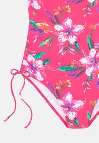 Costume da bagno intero con motivo floreale rosa, caratterizzato da grandi fiori bianchi e colorati, con lacci laterali regolabili e una texture del tessuto liscia.