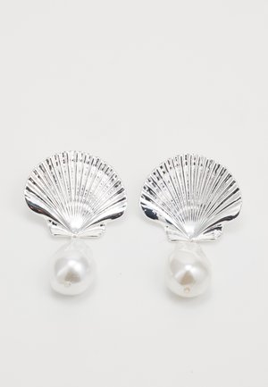 Brincos em forma de concha prateada com grandes pérolas brancas irregulares penduradas abaixo de cada concha, sobre um fundo branco.