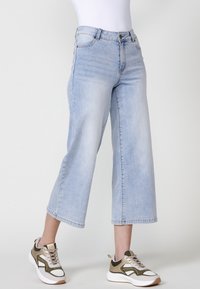 Jeans anchos de color azul claro con cintura alta, que cuentan con cinco bolsillos y corte recto, combinados con zapatillas blancas y oliva.