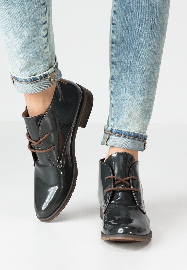 Bottines en cuir verni noir avec des lacets marron, bouts ronds et un petit talon. Portées avec un jean bleu clair retroussé.
