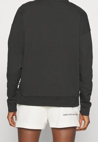 Personne portant un haut à manches longues noir et un short blanc avec le texte « THERE'S ONLY ONE FOREVER » sur la jambe gauche, vue de dos.