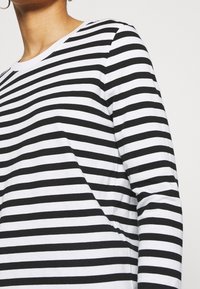 Långärmad randig skjorta i svart och vitt bomull. Har en rundad halsringning och horisontella ränder med lika bredd. Slät textur.