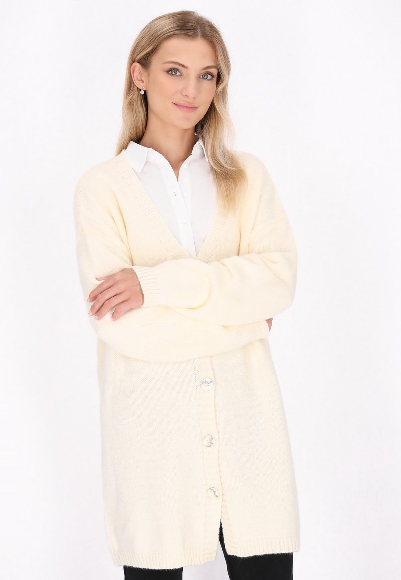 Cardigan lung de culoare crem, cu decolteu în V, mansete cu model în relief și închidere cu nasturi. Țesătură din tricot texturată, cu patru nasturi mari pe partea din față.