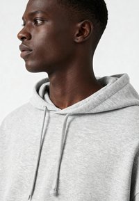 Felpa grigia realizzata in tessuto morbido, con cappuccio regolabile e vestibilità comoda. La texture è liscia con motivi sottili.