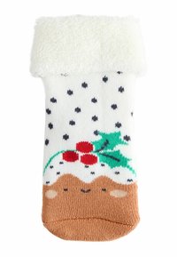 Weißer gestrickter Socke mit schwarzen Punkten, cremefarbenem, flauschigem Bund und festlichem Design, das eine braune Schicht, Stechpalme und rote Beeren zeigt.