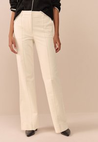 Pantaloni bianchi a gamba larga con dettagli di cuciture verticali. Realizzati in tessuto liscio, presentano una vita aderente e un orlo leggermente svasato. Abbinati a calzature nere.