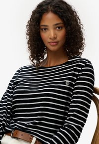 Camisa de manga larga a rayas en blanco y negro, hecha de una tela suave, con un pequeño acento de logo bordado en el pecho.