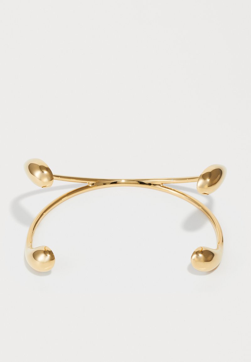 Brazalete de oro con un acabado suave y brillante. Presenta dos extremos redondeados y un diseño minimalista y abierto.