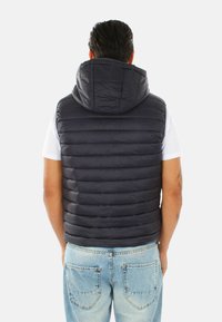 Gilet imbottito di colore blu navy scuro con cappuccio, caratterizzato da segmenti trapuntati per l'isolamento. Completato da un orlo a coste e una finitura liscia e lucida.