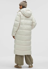 Pikk, koheline valge mantl, millel on kapuuts, horisontaalne õmblus, küljetaskud ja pehme, siledapind. Täiendavad vabalt langevad beežid püksid.