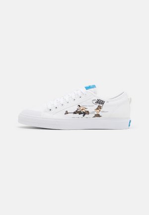 White canvas sneakers with round toe, blue accent on the tongue, and side graphic featuring a character and a checkered flag design.