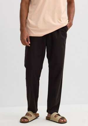 Pantalones negros, ligeros y de corte holgado con una cintura elástica. Combinados con sandalias de color beige con una sola tira y suela de corcho.