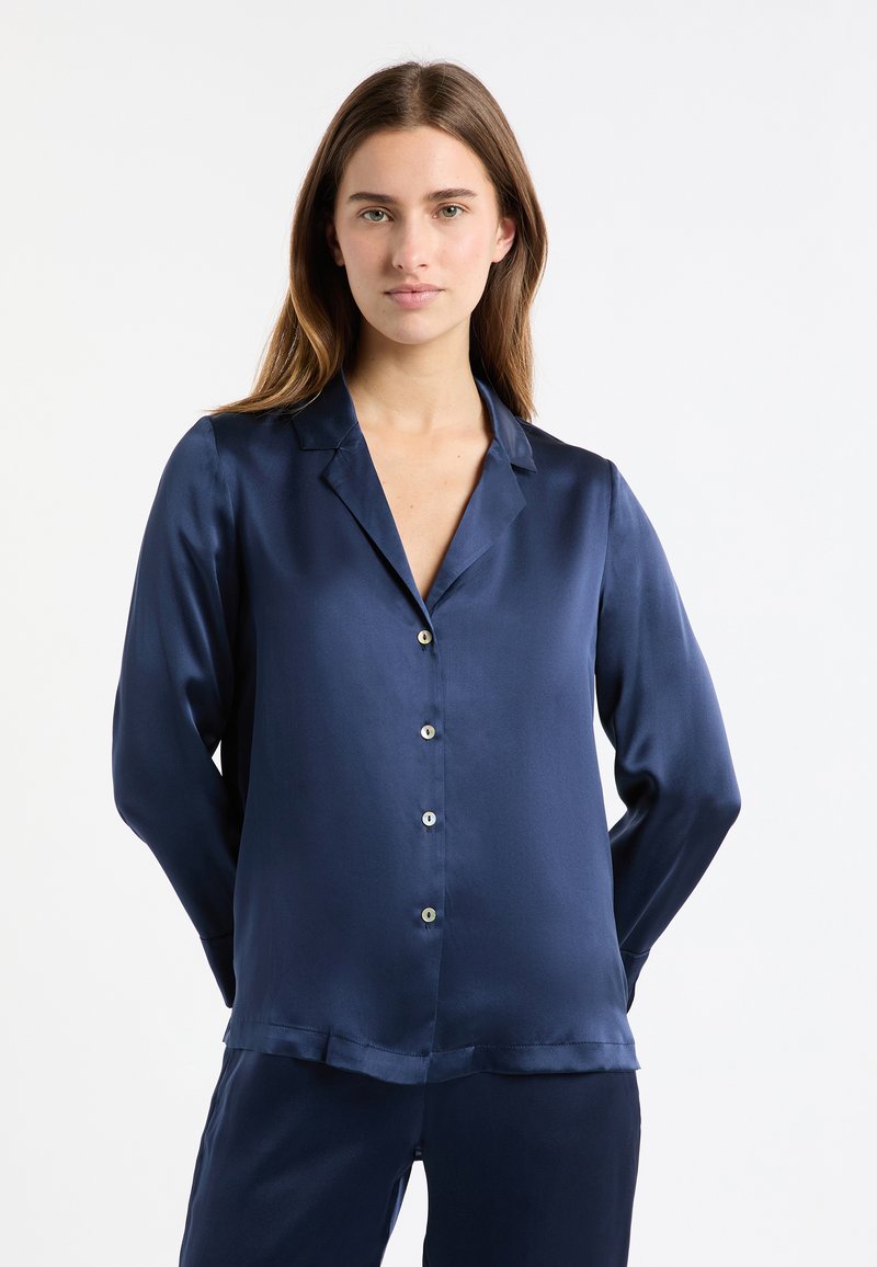 Granatowa satynowa bluzka z długimi rękawami, kołnierzem z wycięciem i zapinana na guziki z przodu. Gładka faktura z subtelnym połyskiem oraz dwoma otwartymi mankietami jako akcenty.