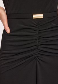 Czarna sukienka z marszczonym materiałem z przodu, tworzącym teksturowany efekt. Złoty metaliczny pasek podkreśla talię. Gładki, elastyczny materiał.