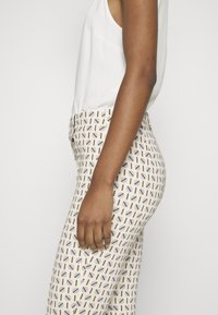 Bukser med en tætsiddende design, der har en cremefarvet bund og multicolore ovale mønstre. Glat stofstruktur med en subtil glans.