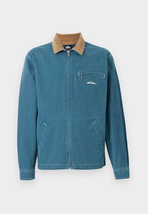 Μπλε ζακέτα με φερμουάρ, καφέ κορδονέ γιακά, δύο κάτω τσέπες και τσέπη στο στήθος με φερμουάρ που έχει μικρό λευκό λογότυπο κύματος.