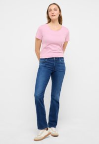 Roze T-shirt met korte mouwen en een ronde hals, voorzien van een reliëflogo, gecombineerd met blauwe denim flared jeans en beige sneakers.