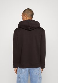 Tmavě hnědá mikina s velkou kapucí, vroubkovanými manžetami a lemem. Tkanina vypadá měkce a má hladký povrch. Jednoduchý, minimalistický design.