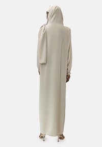 Abito lungo e fluente beige con maniche lunghe e un foulard abbinato. Tessuto morbido, dettagli di drappeggio delicati e polsini elastici.