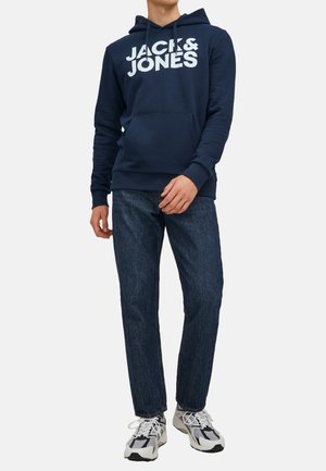 Dunkelblauer Kapuzenpullover mit weißem "JACK & JONES"-Schriftzug, Kängurutasche, gerippte Bündchen und Saum, kombiniert mit dunklen Jeans und Turnschuhen.