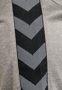 Pullover mit einem hellgrauen Strickmuster und einem schwarzen Stoffeinsatz mit weißen gestreiften Zickzackmustern an der Seite.