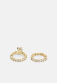 Conjunto de anillos de oro que incluye un solitario con una piedra redonda y una banda de eternidad, ambos adornados con piedras preciosas claras en un diseño texturizado.