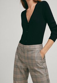 Cardigan noir côtelé avec un décolleté en V profond et une fermeture à boutons, associé à un pantalon taille haute à carreaux avec poches latérales et une coupe décontractée.