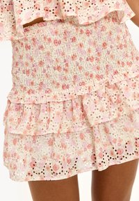 Jupe florale à volants en tissu léger ; possède une taille smockée et un design à couches avec des couleurs rose et crème, ainsi que des détails en œillets.