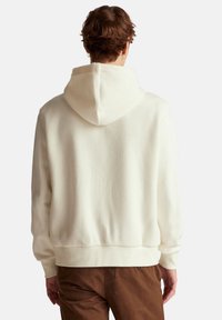 Sudadera con capucha crema de tejido acanalado texturizado, con bolsillo tipo canguro y corte estándar. Presenta una capucha con cordón y puños acanalados.