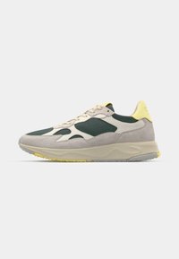 Sport sneakers med en grønn mesh-overdel, beige semsket skinndetaljer, gul hæltab og en tykk, teksturert såle med grå underfot.