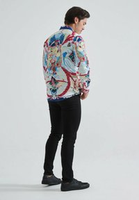 Chemise à manches longues imprimée de fleurs avec une palette de couleurs blanche, bleue et rouge ; associée à un pantalon noir et des chaussures noires ; coupe décontractée.