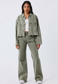 Conjunto de chaqueta y pantalones de mezclilla verde oliva, con un patrón texturizado, diseño cropped, bordes deshilachados y combinado con zapatillas blancas.