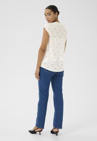 Haut blanc à manches courtes avec un motif de cœurs rouges, associé à un jean droit bleu et des mules à talons noires. Modèle tourné légèrement vers l'arrière.