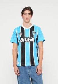 Camiseta de fútbol a rayas azul y negra con cuello en V, que presenta el logo de "alfa", el escudo de Gremio y el logo de Umbro en el lado izquierdo del pecho.