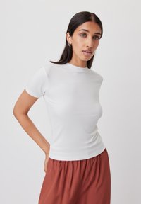 T-shirt bianco a maniche corte, aderente e realizzato in materiale morbido, con collo rotondo e design senza cuciture, abbinato a pantaloni fluenti color ruggine.