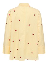 Camisa de manga larga de color amarillo claro con pequeños estampados de fresas rojas dispersas por la tela, vista desde atrás.