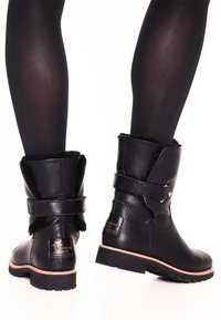 Botas de cuero negro hasta el tobillo con punta redonda, forro de piel sintética, acento de correa cerca de la parte superior y suela exterior resistente para mayor tracción.