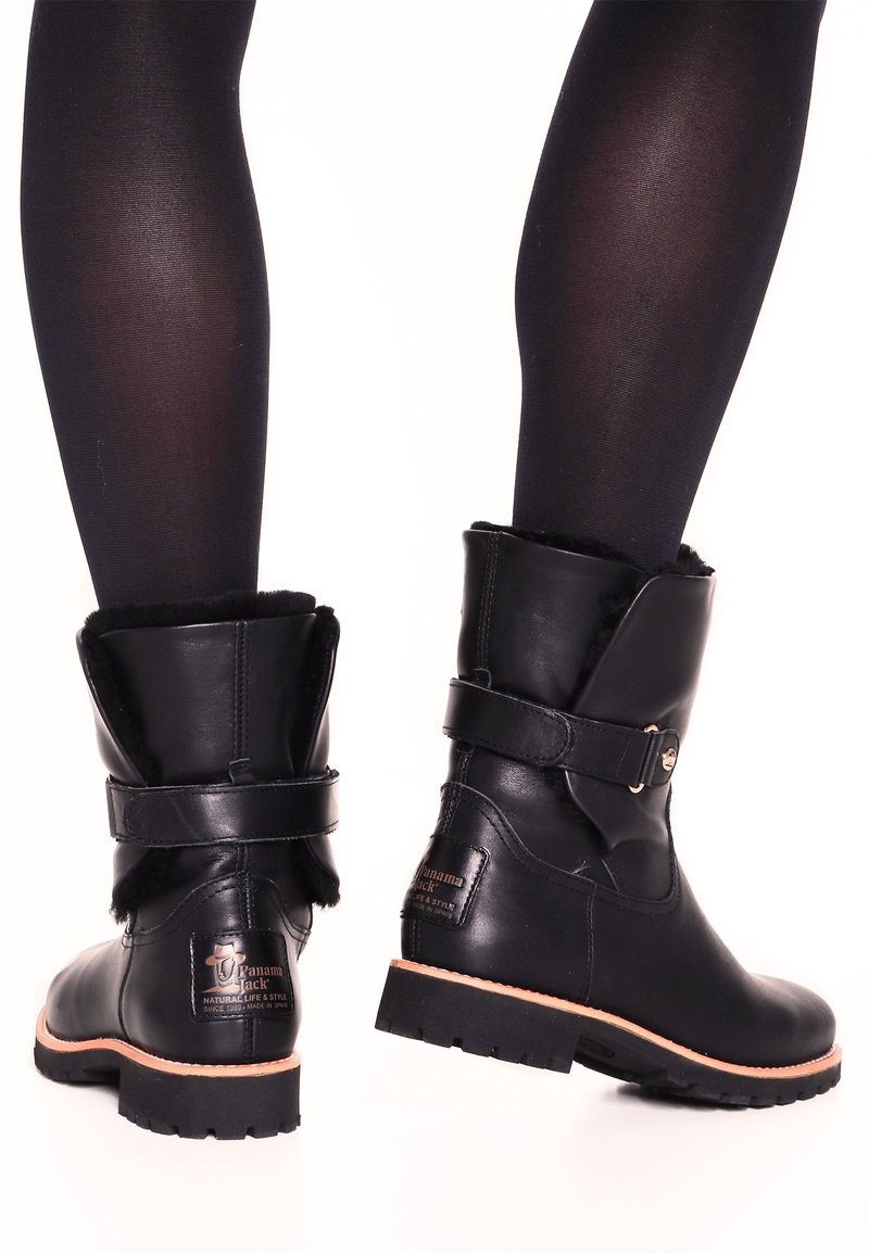 Botas de cuero negro hasta el tobillo con punta redonda, forro de piel sintética, acento de correa cerca de la parte superior y suela exterior resistente para mayor tracción.