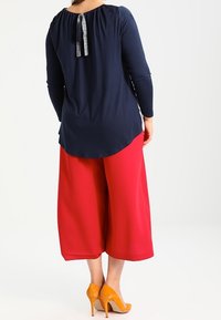 Tämä tummansininen pitkähihaisessa paidassa on gathered kaula-aukko, ja se on yhdistetty leveisiin punaisiin culottiin. Huomionarvoinen yksityiskohta: harmaa nauha paidan takana. Oranssit korot.