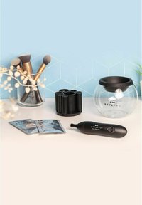 Stylpro sminkborst rengöringskit som inkluderar en svart elektrisk rengörare, en genomskinlig skål, en svart hållare och två blå rengöringsväskor på en ljus yta.