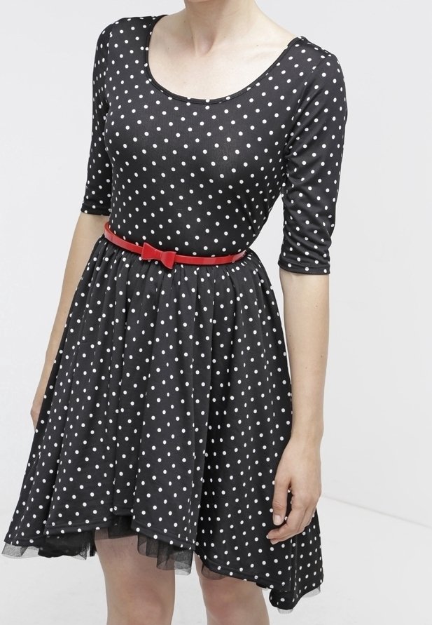 Robe noire à pois blancs, manches trois-quarts, ceinture rouge avec nœud et jupe évasée portée par une personne debout.