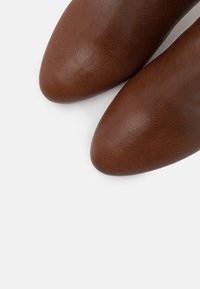 Brune lædersko med en glat tekstur, spids snude og minimalistisk stil. Farven er en dyb, varm brun.