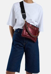 Rode gestikte tas met een meerkleurige gevlochten band en een zwarte verstelbare schouderband. Geverfd over het lichaam met een losse witte T-shirt en denim shorts.