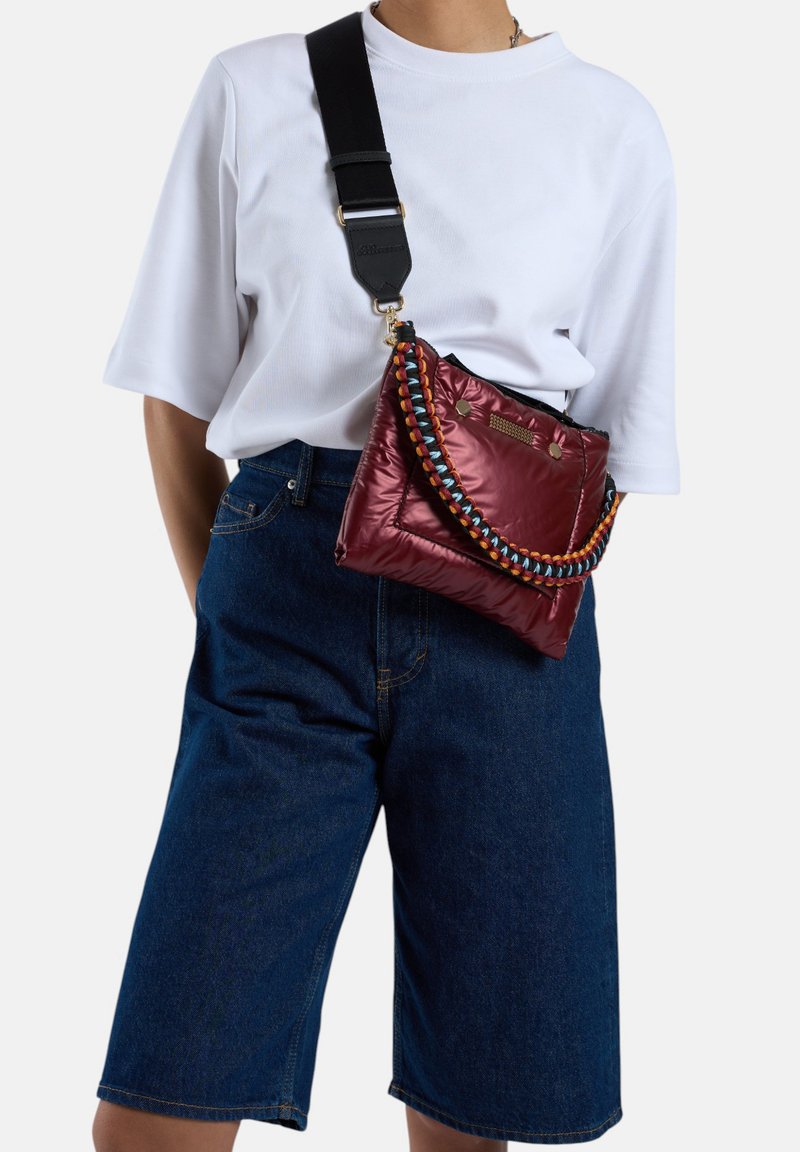 Rode gestikte tas met een meerkleurige gevlochten band en een zwarte verstelbare schouderband. Geverfd over het lichaam met een losse witte T-shirt en denim shorts.