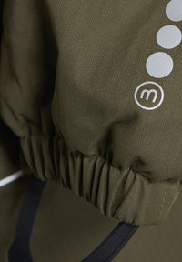 Maslinasto zelena tkanina s uzorkom riblje kosti, sadrži elastični manžet, srebrni logo i pet malih okruglih naglasaka duž strane.