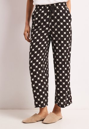 Pantalon court à pois noir et blanc avec taille à cordon, porté avec des chaussures beige facile à enfiler sur une personne debout.