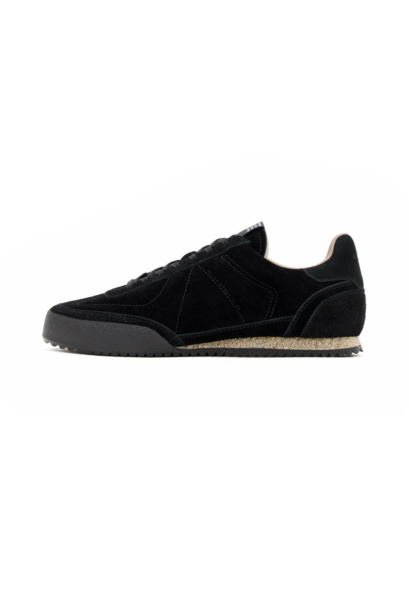Schwarze Wildleder-Sneaker mit einer strukturierten Oberfläche, runder Spitze und einer Gummisohle, die entlang der Mittelsohle einen kontrastierenden sandfarbenen Akzent aufweist.