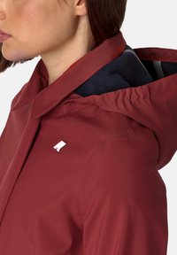 Rood hoodiejack gemaakt van gladde stof, met een omklapbare kraag en zichtbare binnenvoering. Opvallend merkdetail op de borst.