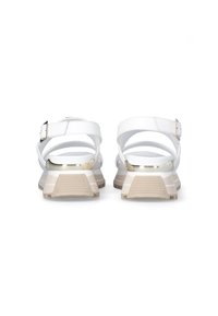 White synthetic sandals with adjustable straps at the ankle, featuring a textured beige and white sole and metallic accent on the heel.